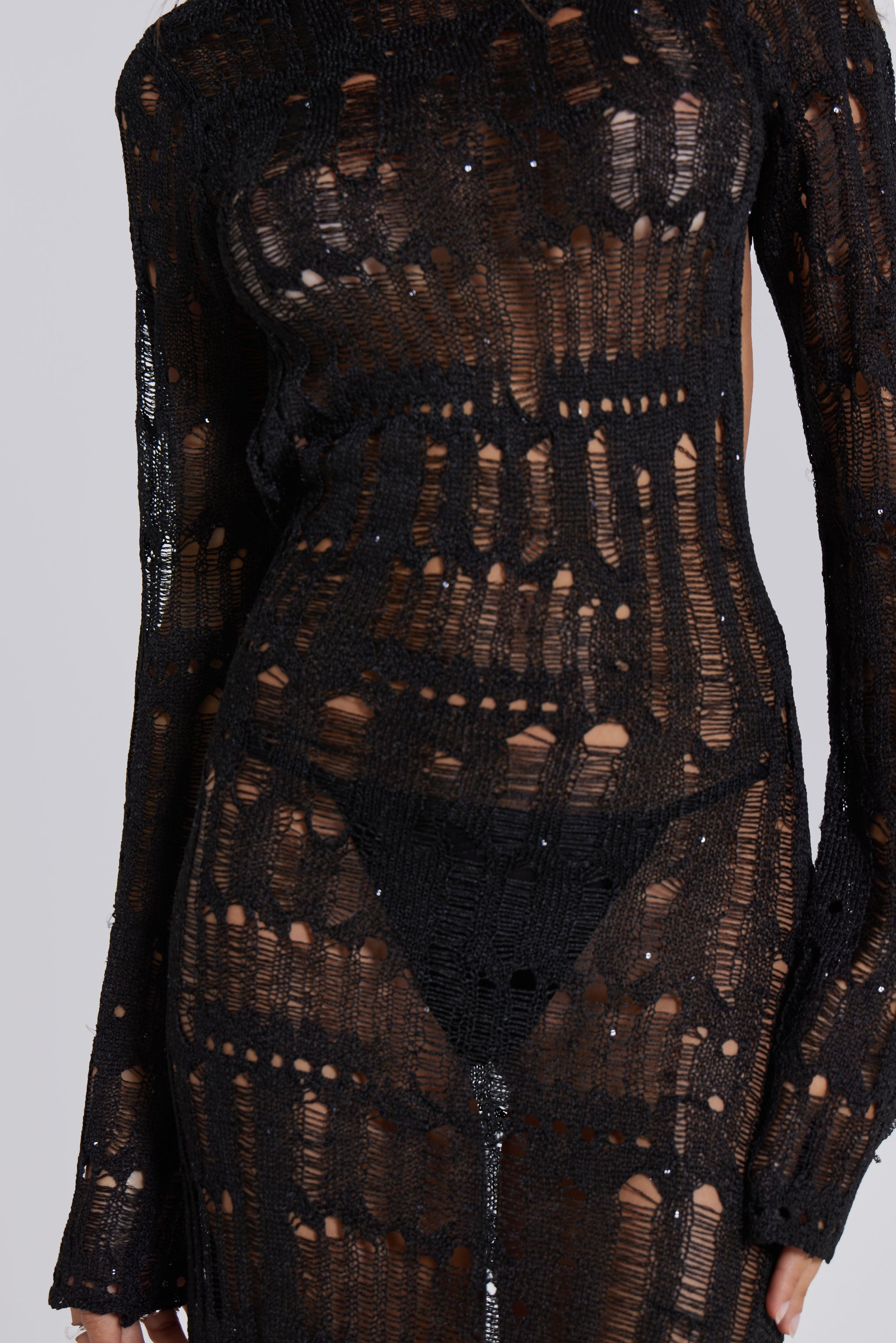 Female model wearing a black shredded, laddered knitted long sleeve maxi dress with sequin details. 