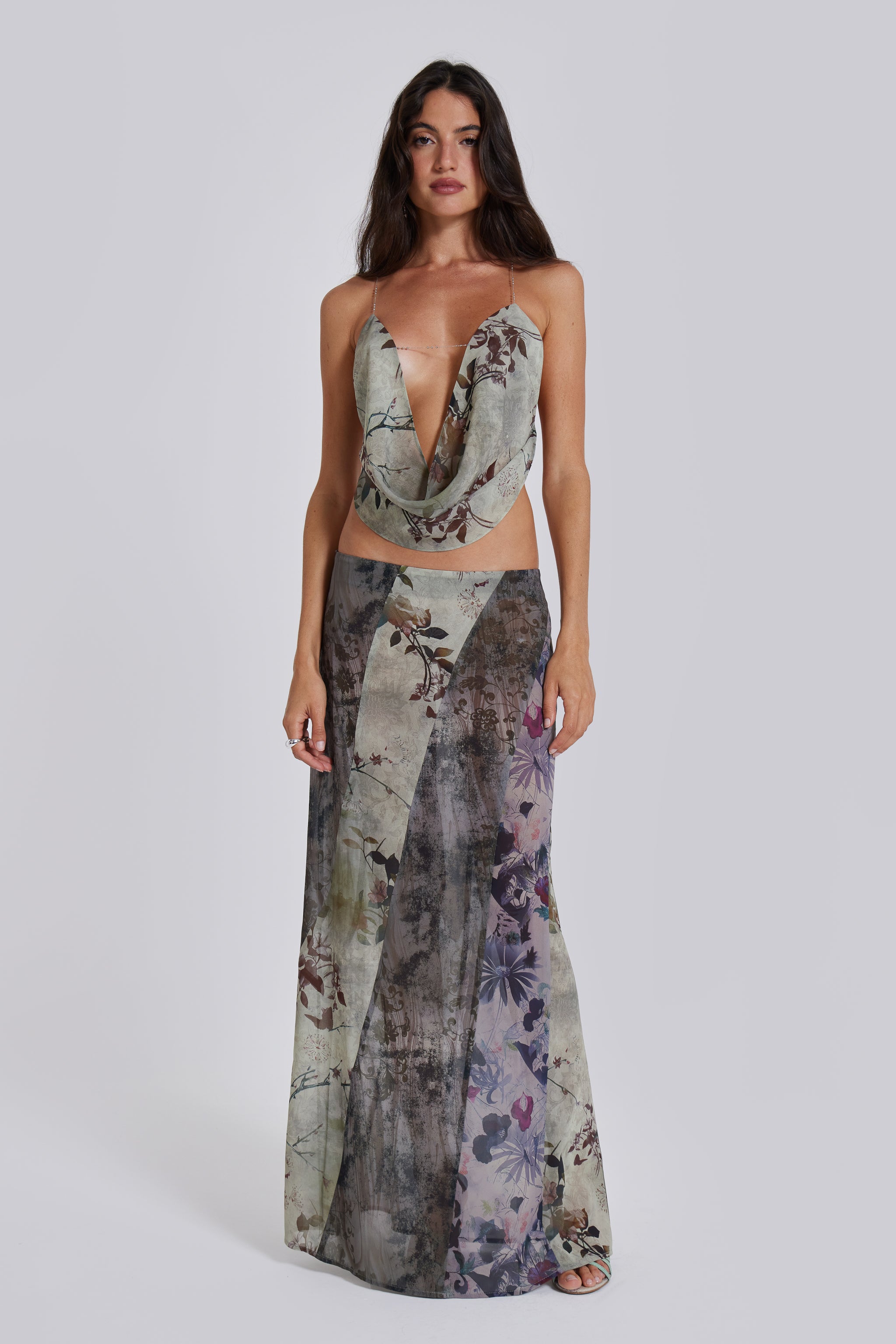 Female model wearing a floral cowl neck backless top with a halter neck chain fastening. Styled with the matching maxi length skirt. 