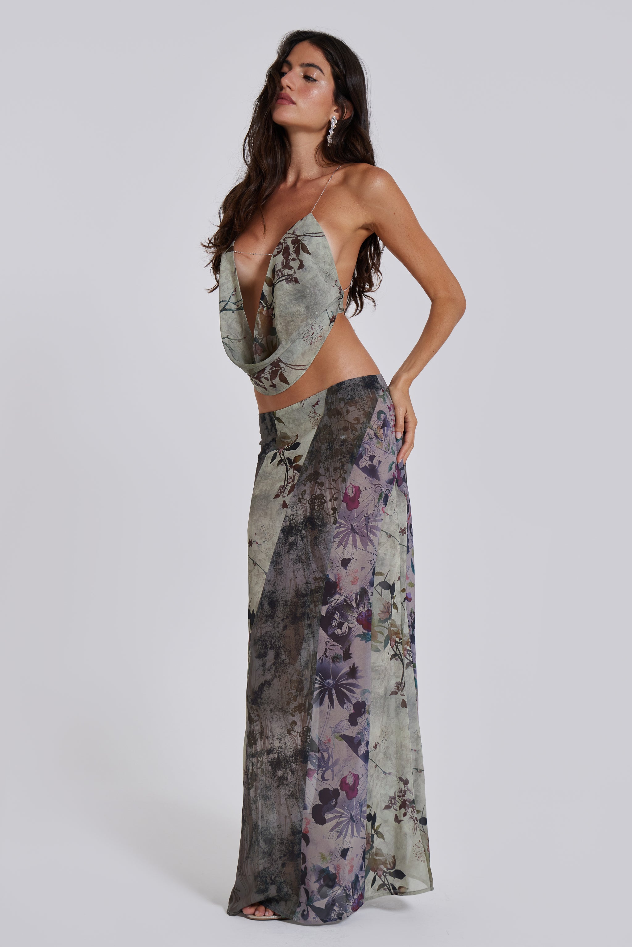 Female model wearing a floral cowl neck backless top with a halter neck chain fastening. Styled with the matching maxi length skirt. 