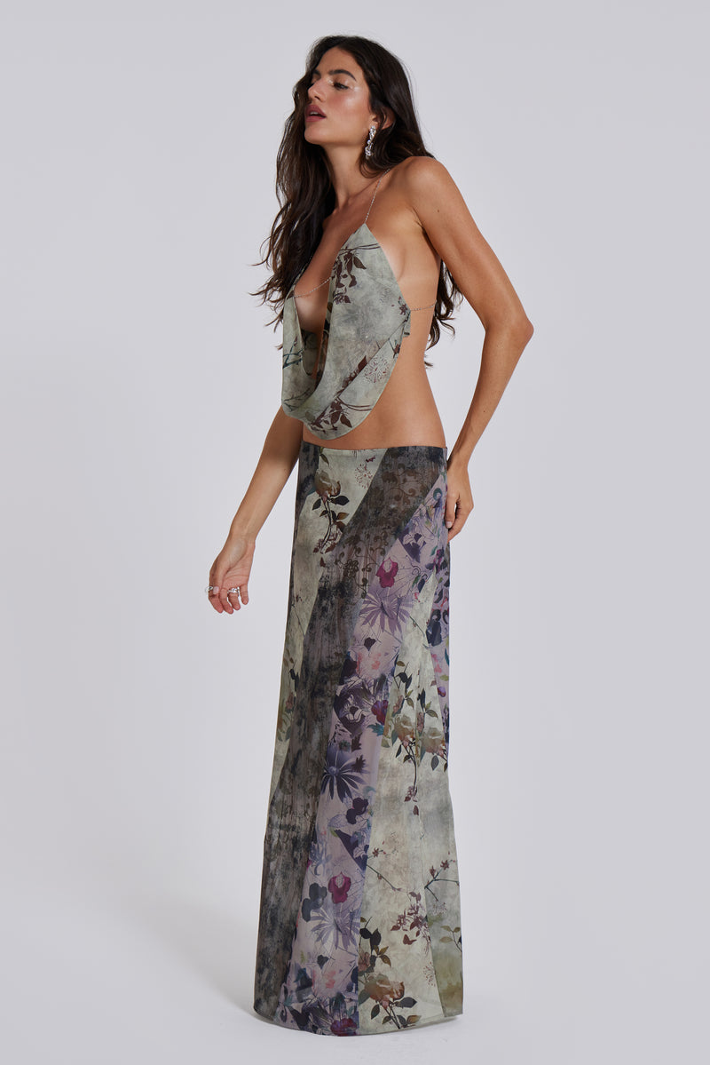 Female model wearing a floral cowl neck backless top with a halter neck chain fastening. Styled with the matching maxi length skirt. 