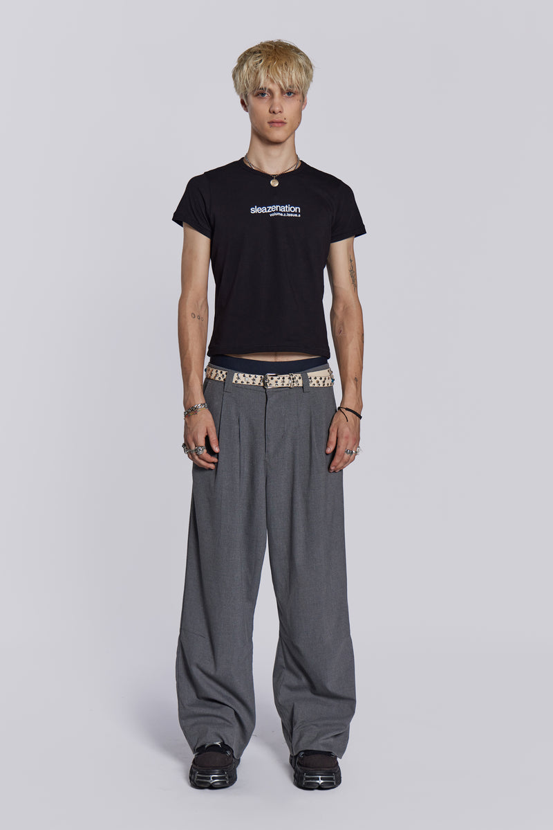 Male wearing black slogan t-shirt, styled with grey pleated trousers, studded belt and boots.