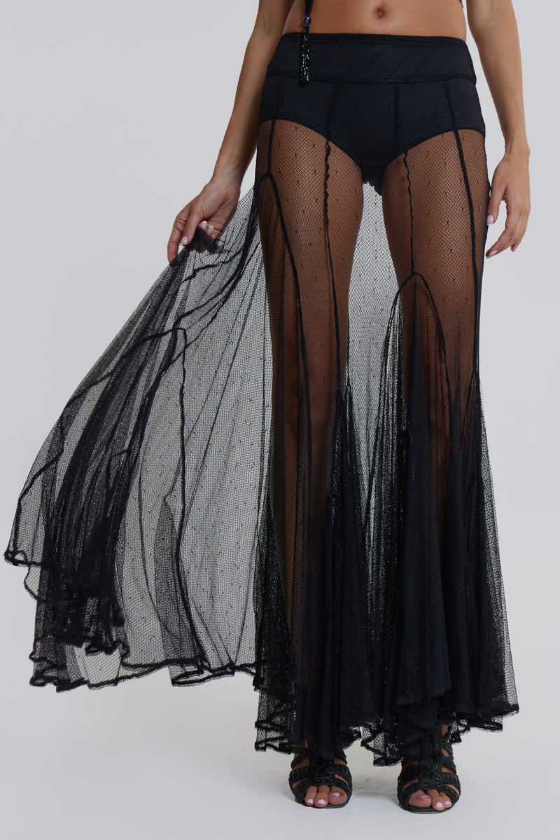 Female model wearing a sheer mesh maxi length skirt in black. Styled with a black and grey graphic one shoulder top. 