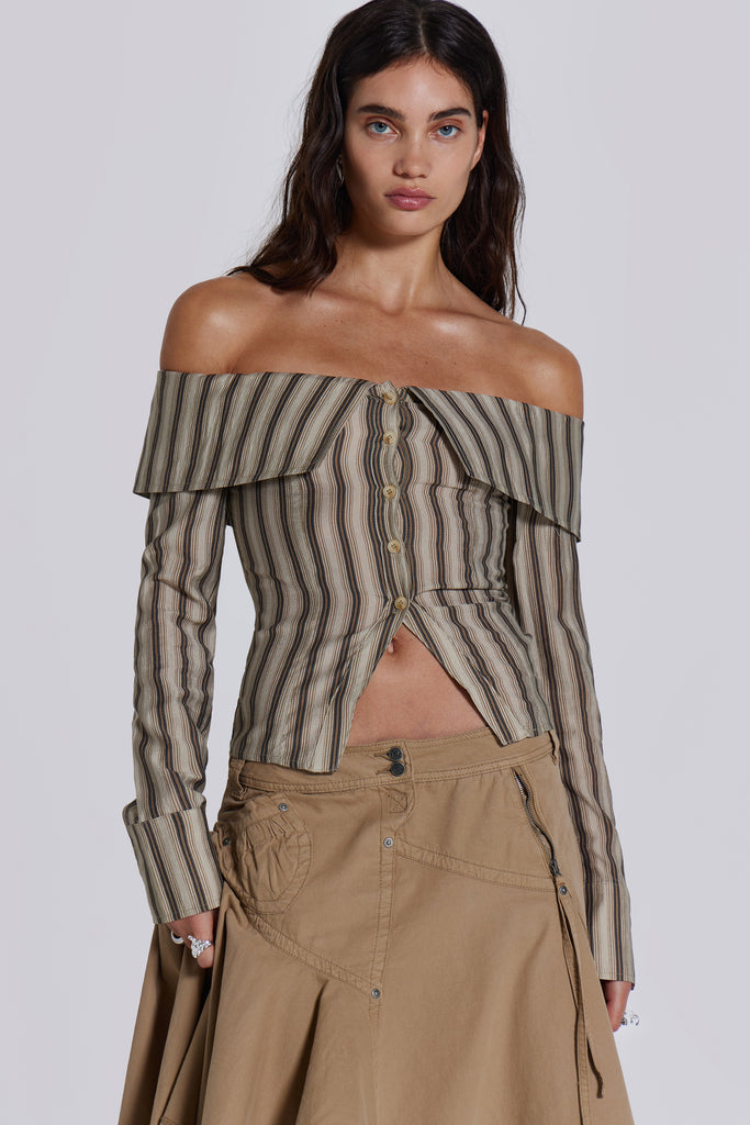  Female model wearing a khaki and brown striped off the shoulder long sleeve shirt with flared cuffs. Styled with a beige choppy cargo skirt. 