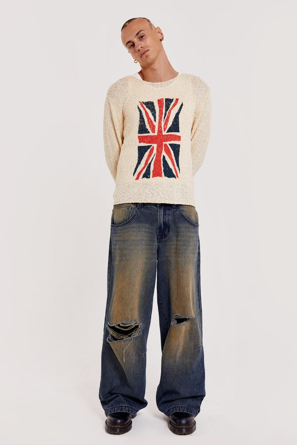 Male wearing white Union Jack printed long sleeve loose knitted crew neck jumper. Styled with sandblast blue denim ripped jeans.