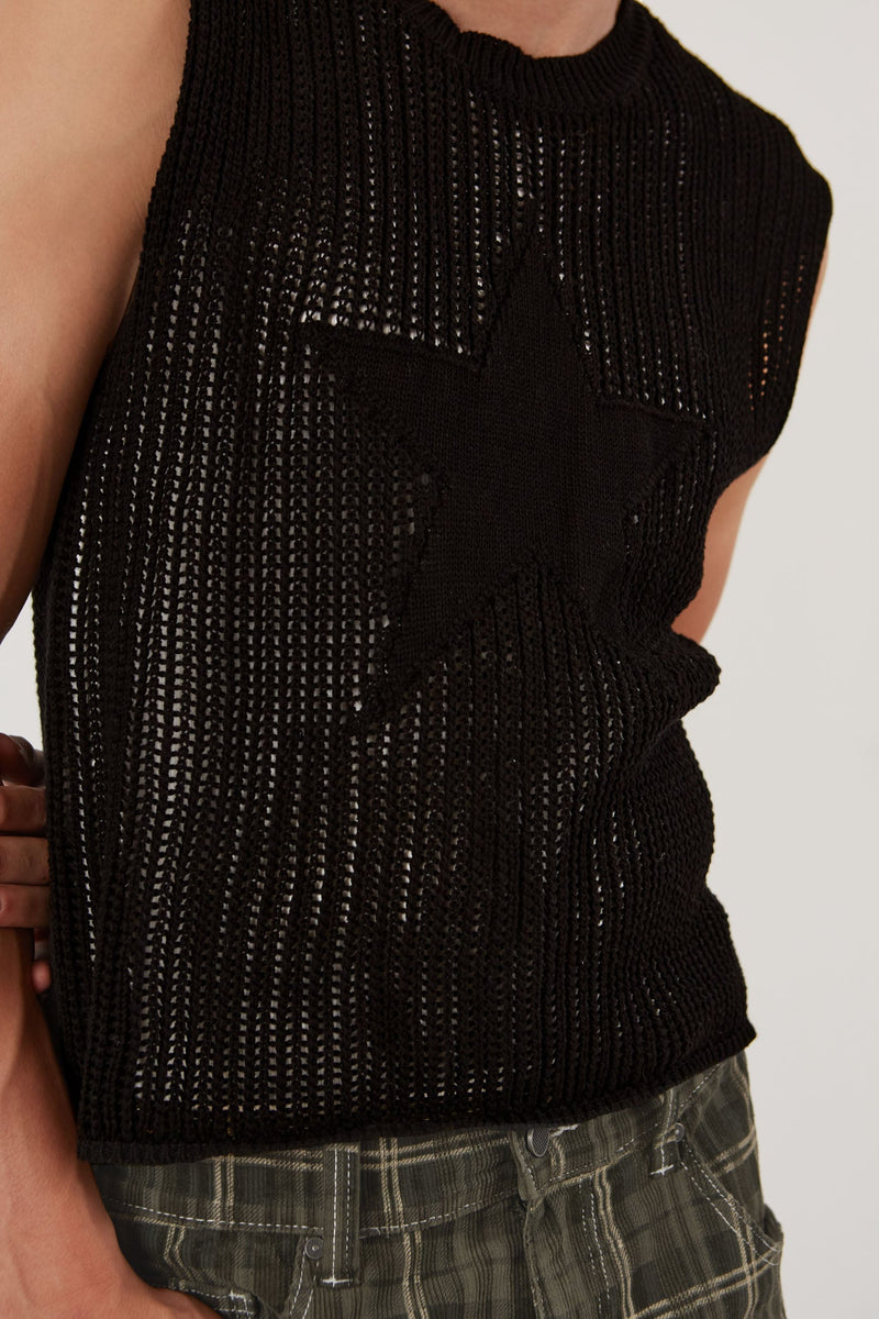Male wearing black sleeveless knitted vest with star detail. Styled with green check oversized shorts.