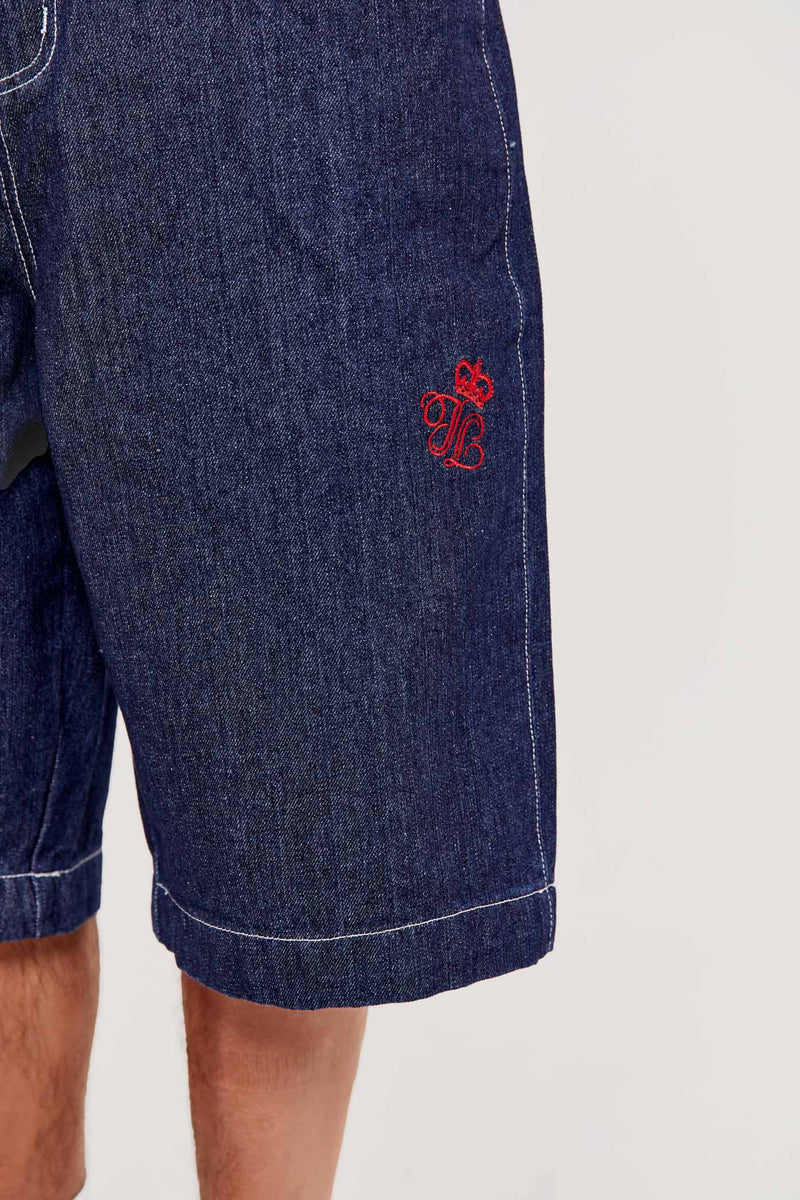 Male wearing indigo blue denim jorts in a jumbo fit with JL embroidered logo and Union Jack start branding on back pocket. 