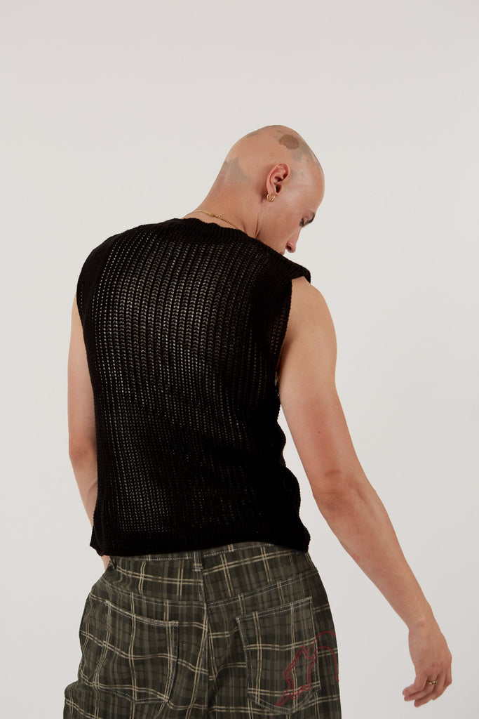 Male wearing black sleeveless knitted vest with star detail. Styled with green check oversized shorts.