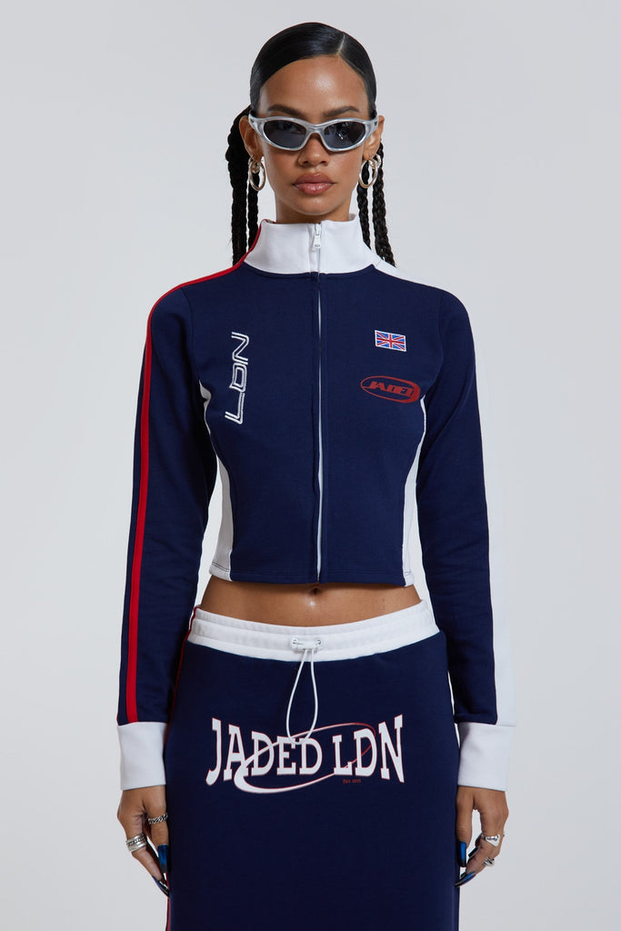 Female wearing navy high neck zip through slim fit long sleeve track top with Jaded branding detail. 