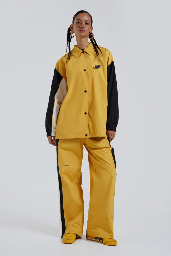 Female wearing yellow oversized drawstring waistband track pants with Jaded branding detail. Styled with the matching track jacket.  
