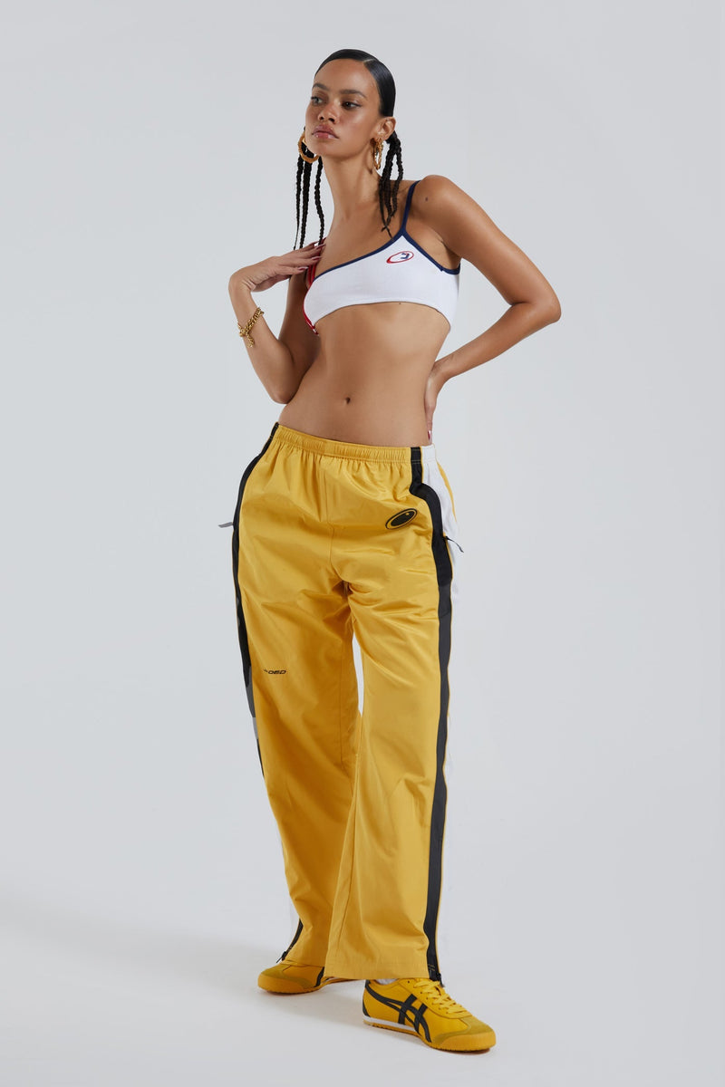 Female wearing yellow oversized drawstring waistband track pants with Jaded branding detail. Styled with a white double strap crop top.