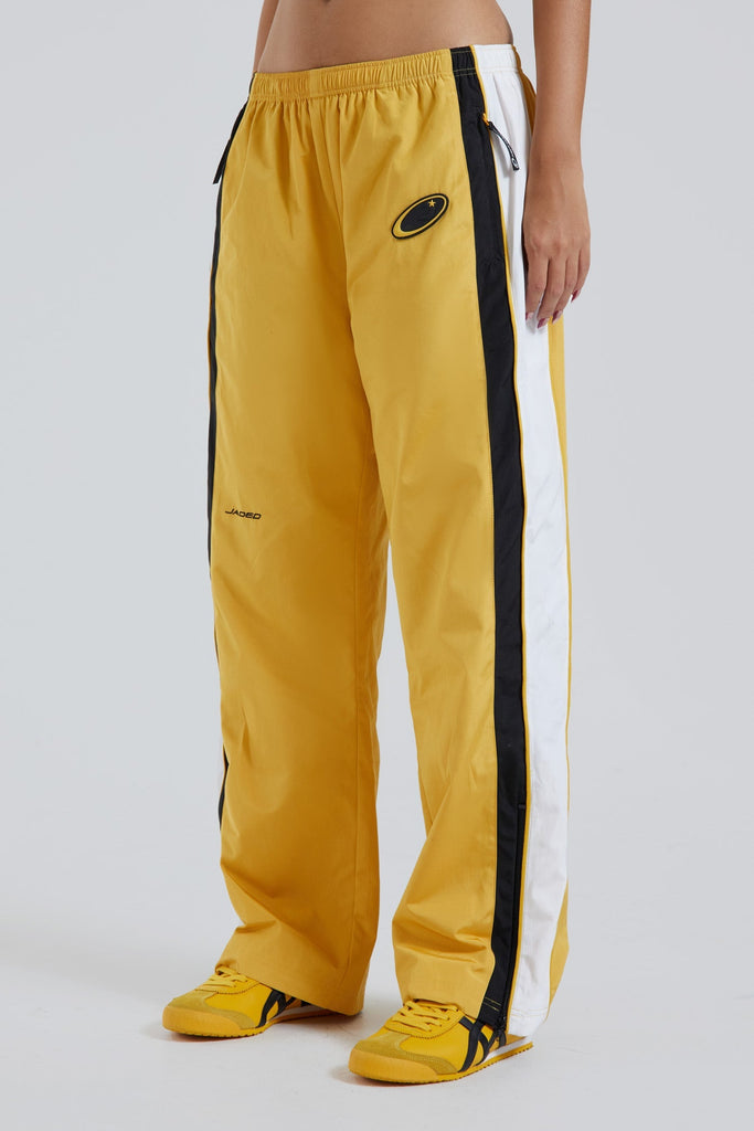 Female wearing yellow oversized drawstring waistband track pants with Jaded branding detail. 