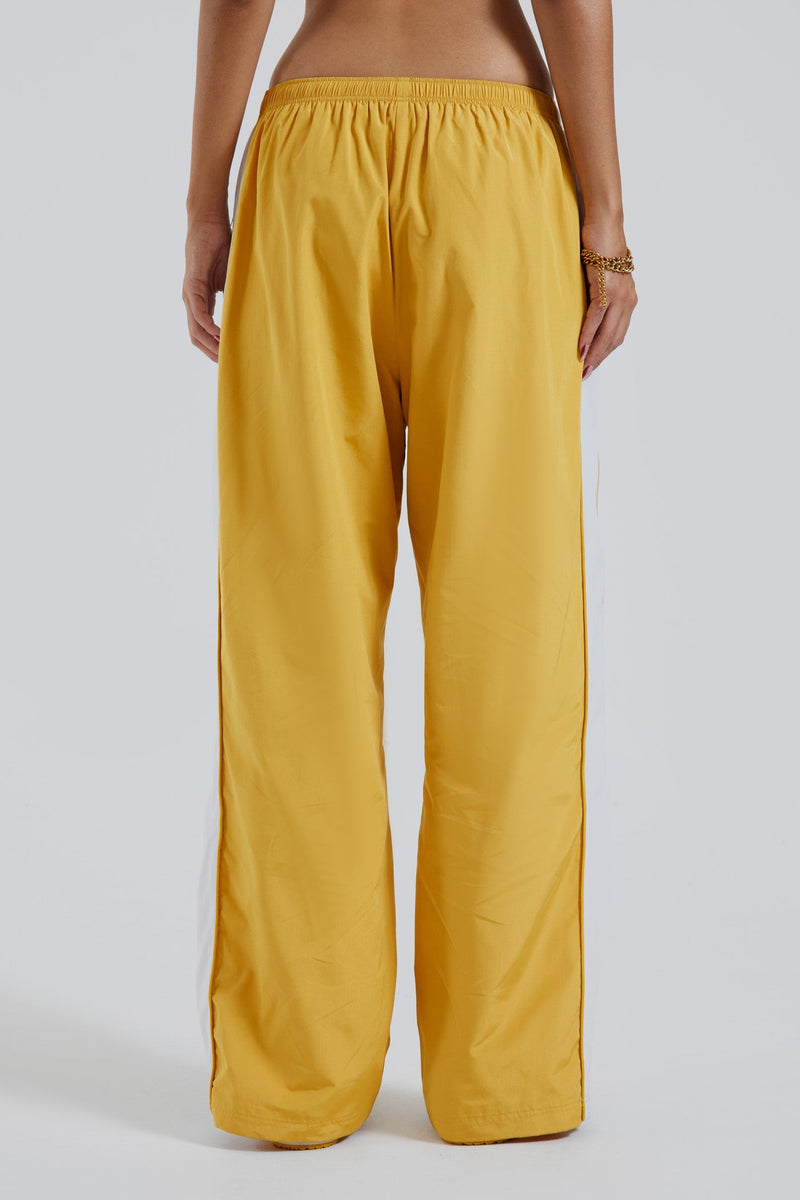 Female wearing yellow oversized drawstring waistband track pants with Jaded branding detail.