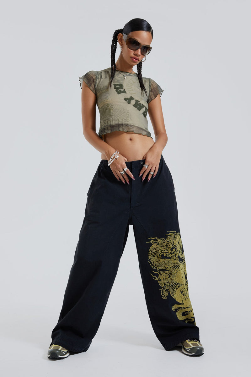 Female wearing black military cargo parachute pants with green dragon flock print. 