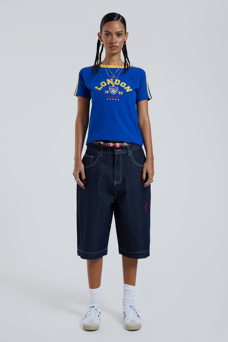 Female wearing sandblast washed denim oversized jorts in a jumbo fit with embroidered pocket patch detail. 