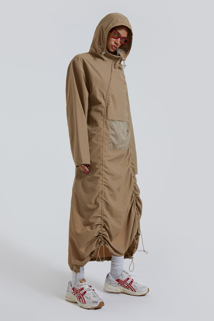 Female wearing stone khaki adjustable ruched detail maxi length long sleeve nylon jacket. 