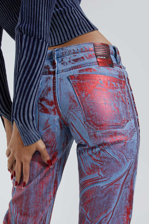Female wearing blue and red distressed foil low rise fit 00’s style jeans. Styled with long sleeve blue knitted cardigan. 