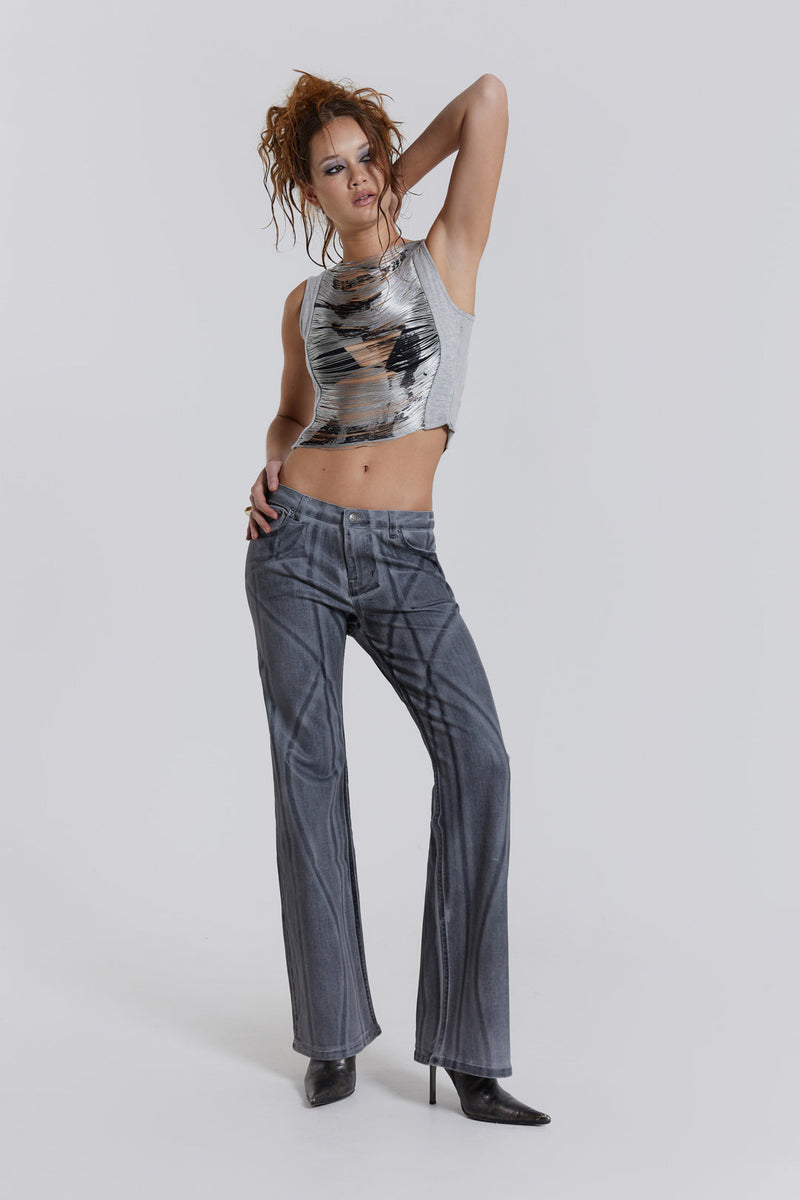 Female model wearing a grey punk collage print sleeveless top with an extreme fringe detail. Paired with grey denim jeans. 