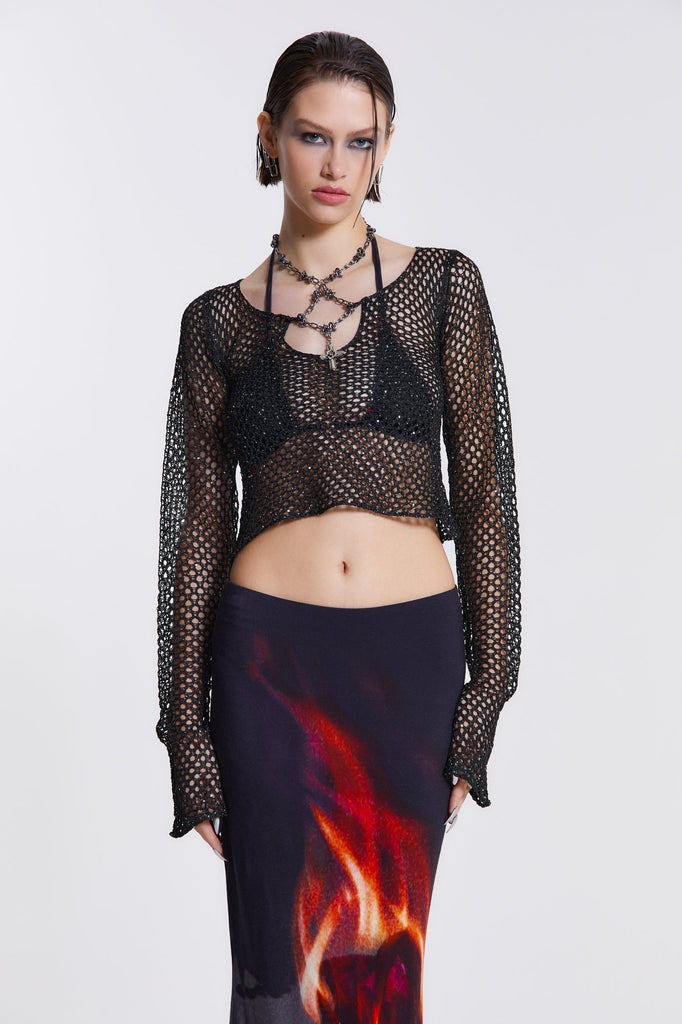 Female model wearing black sequin crochet top which features an attached beaded necklace. The flared sleeves and cropped length can be seen throughout the Vendetta collection. Paired with black wide leg trousers. 